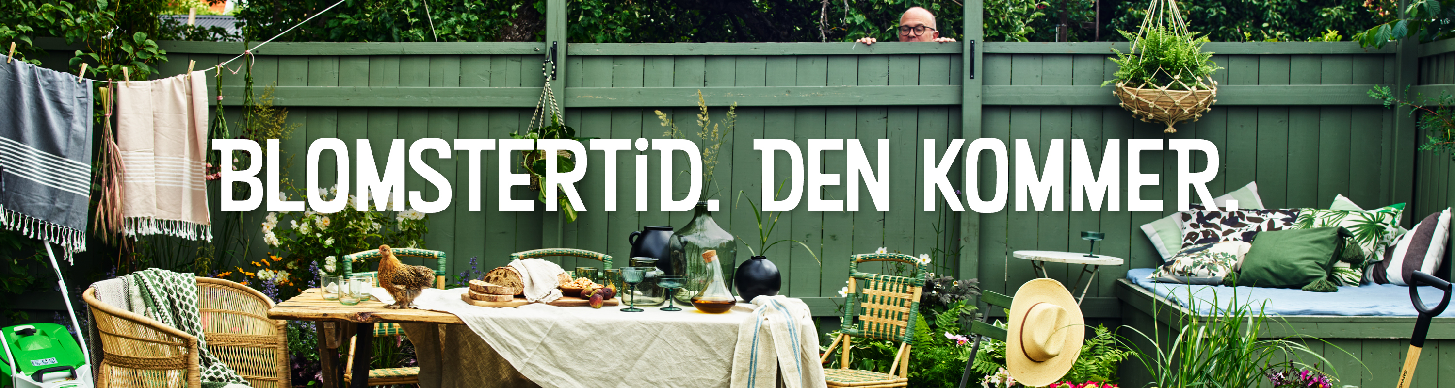 Nordiska trädgårdar - ett grönt staket i bakgrunden, framför syns ett dukat bord, en tvättlina och några stolar.